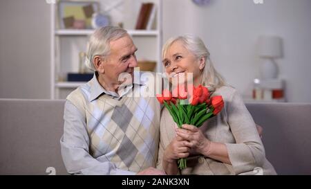 Älterer Mann umarmt glücklich Frau mit Strauß Tulpen, vorhanden Gruß, Aufmerksamkeit Stockfoto