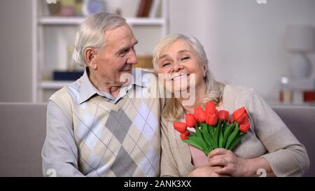 Ältere Paare umarmen zu Hause, Frau mit Bündel von Tulpen, Jahrestag Geschenk Stockfoto