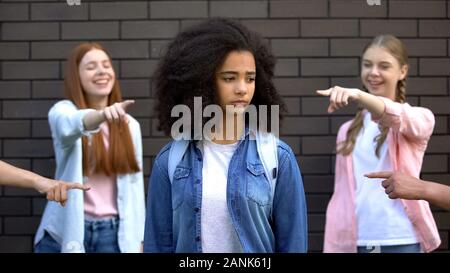 Grausame Gruppe Teens Pointing Finger an Curly afro-amerikanischen Schülerin, Rassismus Stockfoto