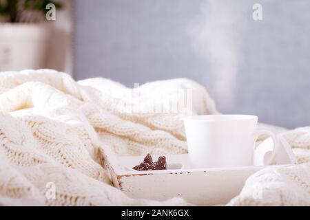 Warme Getränke Tasse mit Schokolade Cookies in einem weißen Wolldecke. Heißes Getränk, gemütlich zu Hause und der kalten Jahreszeit Konzept. Horizontale Stockfoto