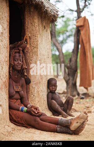 Himba Mutter mit ihrem Kind im Schlamm Haustür sitzend, Kaokoveld, Namibia Stockfoto