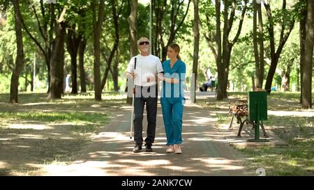 Junge Krankenschwester holding Blinden alten Patienten walking im Park, vision Klinik wiederherstellen Stockfoto