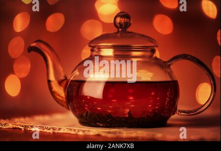 Teekanne aus Glas auf dunklem Hintergrund mit goldenen Bokeh leuchtet Stockfoto