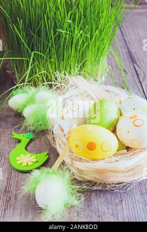 Frühjahr Zusammensetzung mit einem korbsieb Nest aus Stroh, grünes Gras, dekorativen Vogel und Osterei auf einer soliden Holz- Hintergrund. Stockfoto