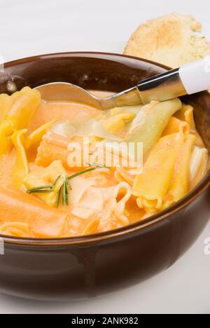 Rainbow hausgemachte Pasta und Tomaten Suppe serviert in einem braunen Schale mit geröstetem Brot auf der Seite. Stockfoto