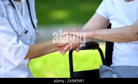 Weibliche Krankenschwester die Hand der behinderten Frau im Rollstuhl, fürsorgliches Personal Stockfoto