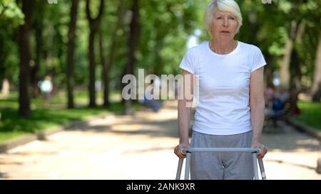 Traurig behinderte Frau mit Rahmen walking im Park, Rehabilitation nach Trauma Stockfoto