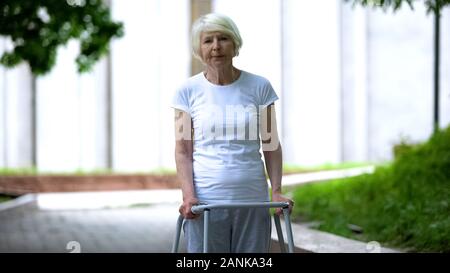 Traurige alte Frau mit Gehhilfe bei Sunny Krankenhaus Park, unwirksame Behandlung Stockfoto