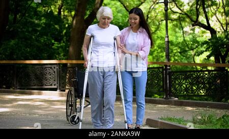 Weibliche Freiwillige helfen behinderten älteren Frau, Spaziergang im Park, Support Stockfoto