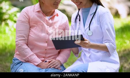 Gerne weibliche Arzt im Alter von Patienten suchen Tablet sitzen draussen, Technologie Stockfoto
