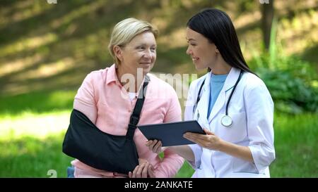 Asiatischen medizinischen Arbeiter mit Tablet lächelnd zu verletzten älterer Patienten im Arm Schlinge Stockfoto