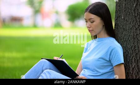 Studentin Essay schreiben, Sitzen, Park, Journalist Artikel, Notizen Stockfoto
