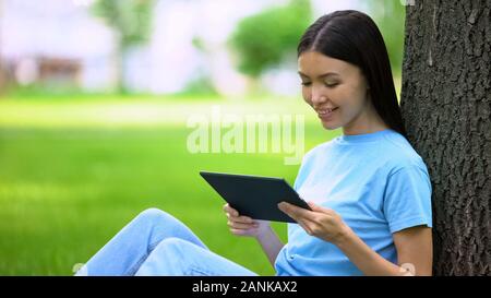 Attraktive junge Frau beobachten Tablet video sitting park, On-line-Anwendung Stockfoto