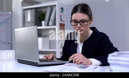 Weibliche Mitarbeiter durch Informationen in Laptop und Dokumente, Arbeiten Stockfoto