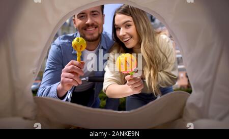 Fröhliche Mamma und Vati schütteln Spielzeug vor der Neugeborenen im Pram Rattle, Elternschaft Stockfoto