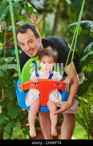 Vati mit jungen Tochter spielen auf Swing im Green Park Stockfoto