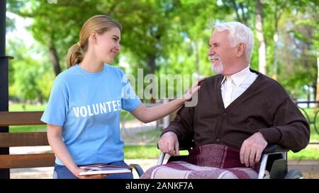 Weibliche freiwillige Holding Buch verbringt Zeit mit behinderten älteren Mann im Park Stockfoto