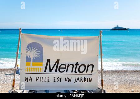 Die Flagge und Emblem für Menton, Frankreich, das übersetzt, y Stadt bin ist mein Garten', Fliegen an einem Strand entlang das Mittelmeer an der französischen Riviera Stockfoto