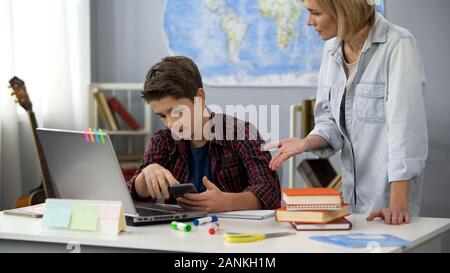 Männliche Teenager mit Telefon ignorieren umgekippt Mutter, Hausaufgaben, Gleichgültigkeit, Bildung Stockfoto