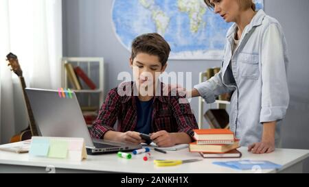 Mama mit Sohn mit Smartphone statt Hausaufgaben, Erzeugung Abstand Stockfoto