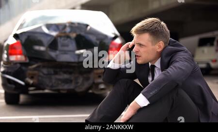 Besorgt man am Telefon sprechen im Freien gebrochen Auto Hintergrund, Verkehr Zusammenstoß Stockfoto