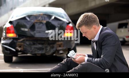 Junger Mann zählen Dollar City Road auf Defekten Auto Hintergrund, Autounfall Stockfoto