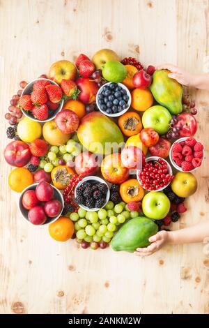 Hand Kreis des Kindes aus Früchten und Beeren, Orangen, Pflaumen Erdbeeren Himbeeren Äpfel, Kiwis, Weintrauben, Heidelbeeren mango Papaya auf Holztisch, Ansicht von oben, Kopieren, selektiven Fokus Stockfoto