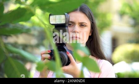 Frau mit Kamera versteckt hinter Bäumen, Journalist auf der Suche nach Sensation Stockfoto