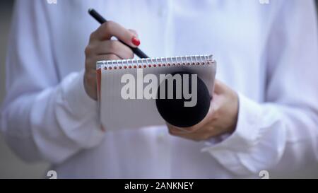 Journalist mit Mikrofon Schreiben von Daten im Notebook, Vorbereitung Zeitungsartikel Stockfoto