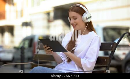 Happy rothaarige Mädchen im Headset hören die Musik auf Tablet outdoor, Ruhezeit Stockfoto