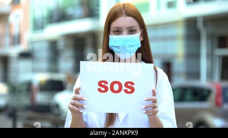 Junge Frau in Schutzmaske Holding sos-Zeichen, Luftverschmutzung, Treibhausgasemissionen Stockfoto