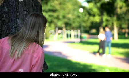 Frau auf der Suche nach paar Walking outdoor Datum versteckt sich hinter Baum im Park Stockfoto