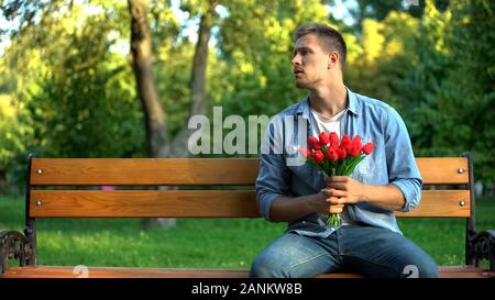 Sorgen Mann mit Bündel Tulpen wartende Freundin für Datum auf der Bank im Park Stockfoto