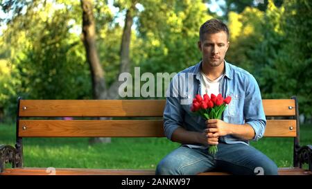 Junge männliche mit roten Tulpen sitzen Parkbank warten auf Freundin Datum, Liebe Stockfoto