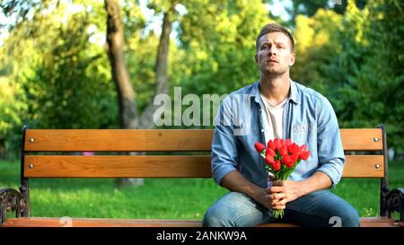 Warten stattlicher Mann mit roten Blüten sitzen Parkbank, outdoor Datum Zuneigung Stockfoto