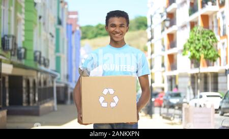 Happy mixed-race jugendlich männlichen eco - Freiwilliger holding Papierschachtel mit Recycling Zeichen Stockfoto