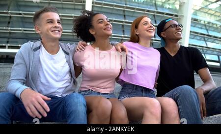 Fröhliche Teenager Freunde umarmen sitzen Stadion zusammen, gemischtrassig Studenten Stockfoto