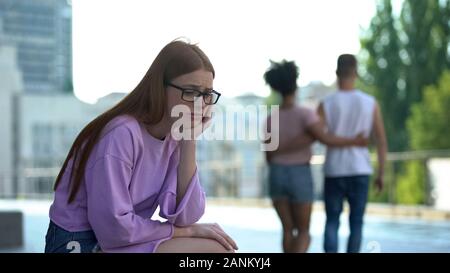 Deprimiert redhead jugendlich alleine während liebende Paar vorbei auf der Straße sitzen Stockfoto