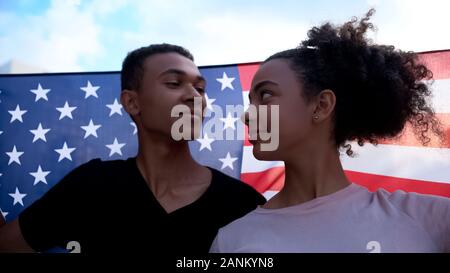 Fröhliche gemischtrassig Studenten in Liebe Holding USA Flagge suchen einander, März Stockfoto