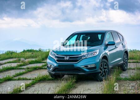 Mnt. Runa, Ukraine - May 22, 2019: Blau suv auf einer gepflasterten Wiese. Beliebte AWD Fahrzeug in der Natur Landschaft. stürmisches Wetter mit bewölktem Himmel. Ihrer Familie Stockfoto