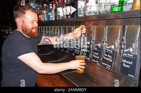 Lächelnd Barkeeper zieht ein Pint, in einem Handwerk Bier Bar, mit vielen Handwerk Bier Taps, Edinburgh, Schottland, Großbritannien Stockfoto