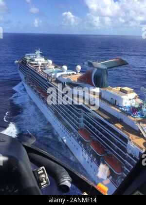 Ein Coast Guard Air Station Borinquen MH-65 Dolphin helicopter Crew fliegt über das Kreuzfahrtschiff Carnival Pride, etwa 75 km nördlich von San Juan, Puerto Rico, Jan. 16, 2020. Die Küstenwache medevaced ein 34-jaehriger Mann aus dem Kreuzfahrtschiff Carnival Pride, etwa 75 km nördlich von San Juan. (Küstenwache Foto) Stockfoto