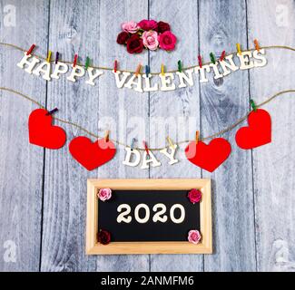 Happy Valentines Tag mit roten Herzen und Blumen auf einem Holz Hintergrund mit 2020 auf einer Schiefertafel Stockfoto