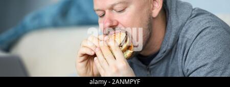 Mann sitzen auf dem Sofa und Burger essen gegen flach Stockfoto