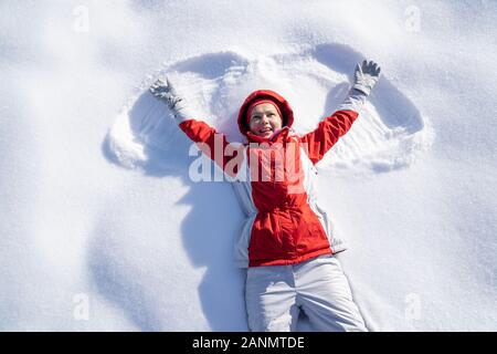 Hohe Betrachtungswinkel und einer verspielten jungen Frau liegend auf Schnee genießen Sie während Ihrer Ferien Stockfoto