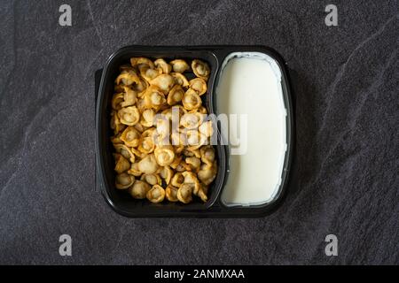 Nehmen russische Pelmeni gebratene Knödel mit Fleisch, Joghurt, Tomatensauce und Gewürze in Plastik Box Container/Paket. Traditionelle gesundes Essen. Stockfoto