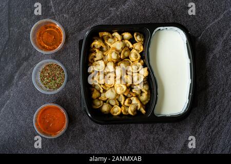 Nehmen russische Pelmeni gebratene Knödel mit Fleisch, Joghurt, Tomatensauce und Gewürze in Plastik Box Container/Paket. Traditionelle gesundes Essen. Stockfoto