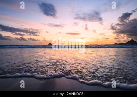 (Selektive Fokus) Atemberaubende Aussicht auf Wellen, die an einem schönen Strand in einer dramatischen und romantischen Sonnenuntergang. Stockfoto