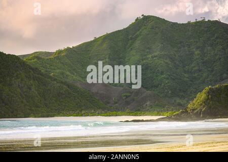 Atemberaubende Aussicht auf die selong Belanak Strand durch eine grüne bergige Küste bei Sonnenuntergang flankiert. Stockfoto