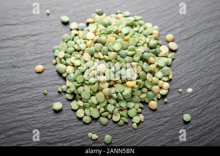 Trocken grüne Erbsen auf einem schwarzen Schiefer Hintergrund verstreut. Bohnen für nahrhafte Suppe Stockfoto